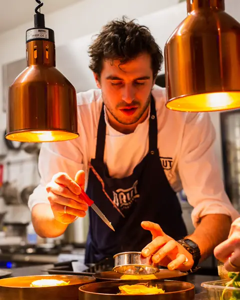 Chef plating a dish under warm kitchen lamps